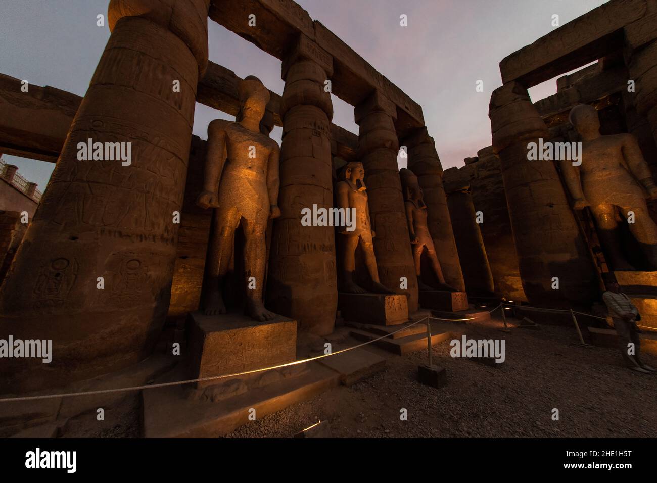 Statuen und Säulen im Luxor-Tempel in Ägypten, die am Abend durch Lichter beleuchtet werden, wenn die Dunkelheit fällt, was einen wunderschönen und dramatischen Effekt bewirkt. Stockfoto