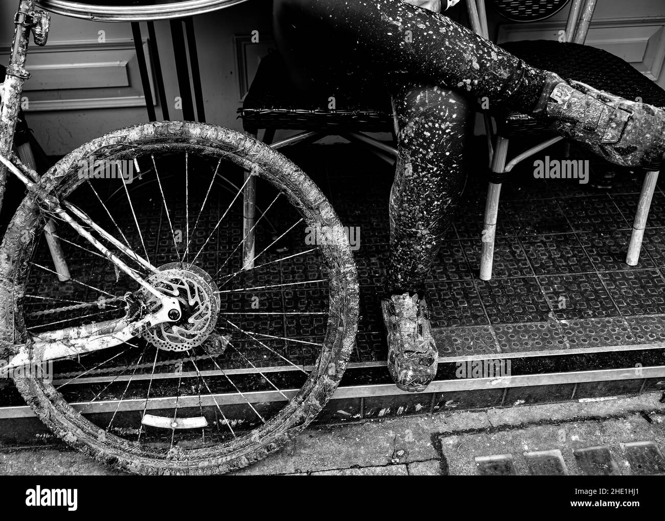 Mann, der sich in einem Straßencafé entspannt hat, nachdem er auf seinem Cross Country Bike richtig schlammig geworden war Stockfoto