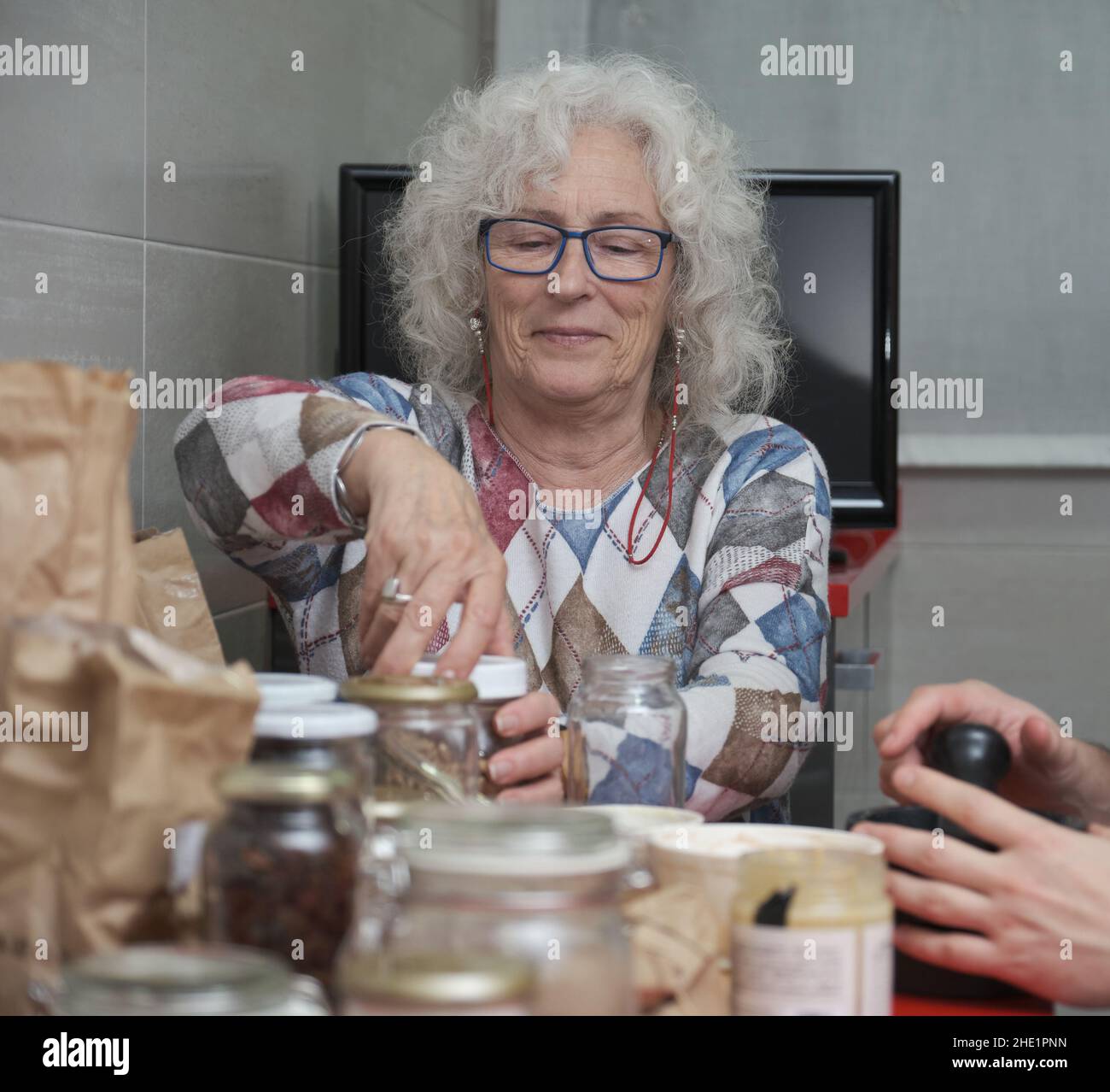 Reife Frau öffnet ein Glas, während sie Süßigkeiten in der Küche zubereitet. Stockfoto