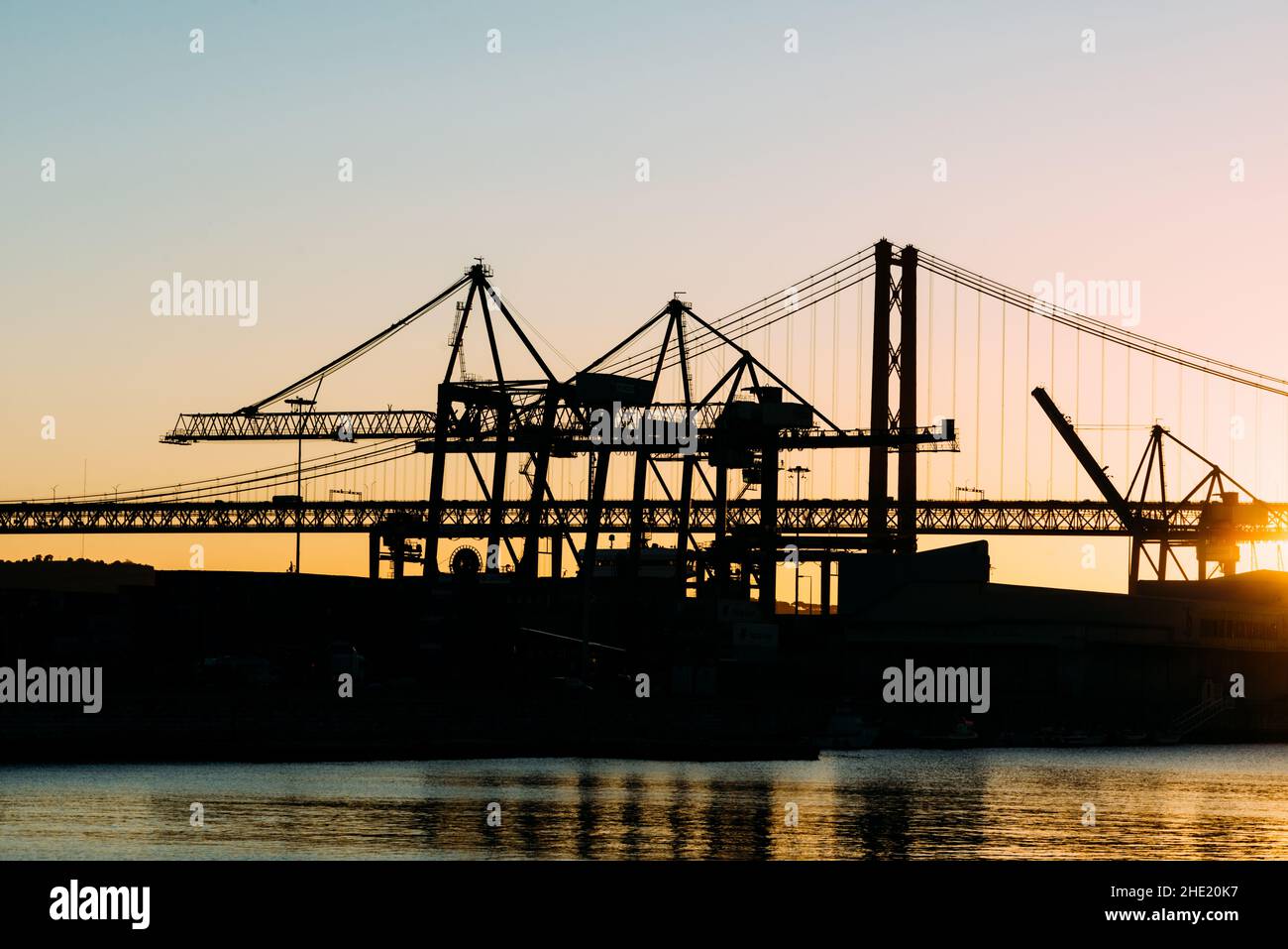 Silhouette von Kränen im Hafen von Lissabon, Portugal mit der Brücke vom 25. April im Hintergrund bei Sonnenuntergang Stockfoto