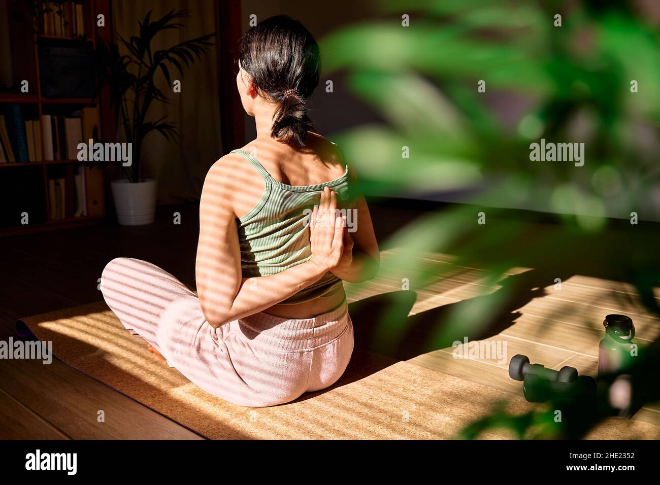 Frau in Gomukhasana- oder Kuhgesicht-Pose sitzend in Lotuspose auf Yogamatte. Wohlbefinden. Achtsames Meditationskonzept. Wohlbefinden. Yoga zu Hause üben. Stockfoto