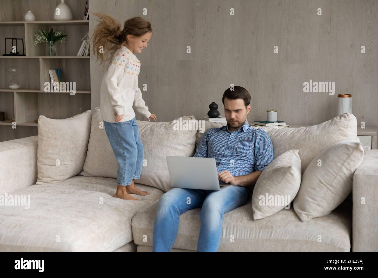 Konzentrierter junger Vater arbeitet, während kleines Kind spielt. Stockfoto