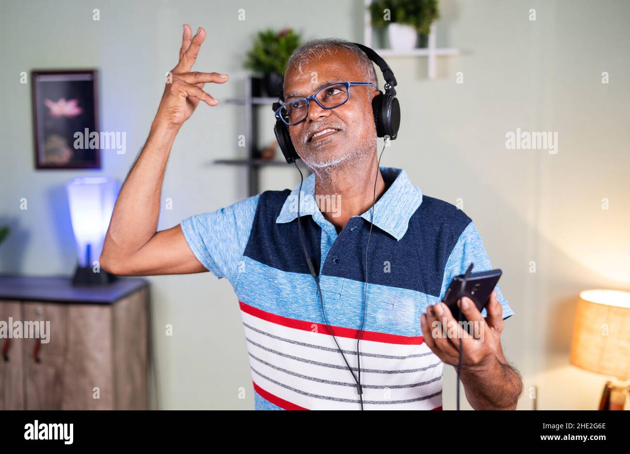 Aktiver älterer Mann mit Kopfhörern, der zu Hause Musik auf dem Mobiltelefon hört – Konzept eines gesunden, flauen Lebensstils, Freudvoll und Entspannung Stockfoto