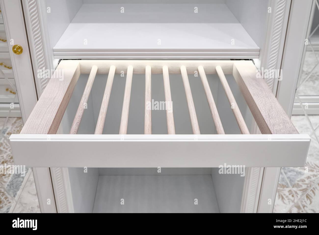 Eleganter weißer Schrank mit offenem leerem ausziehbarem Gestell für Hosen und LED-Beleuchtung in luxuriösem begehbarem Schrank, Nahsicht Stockfoto