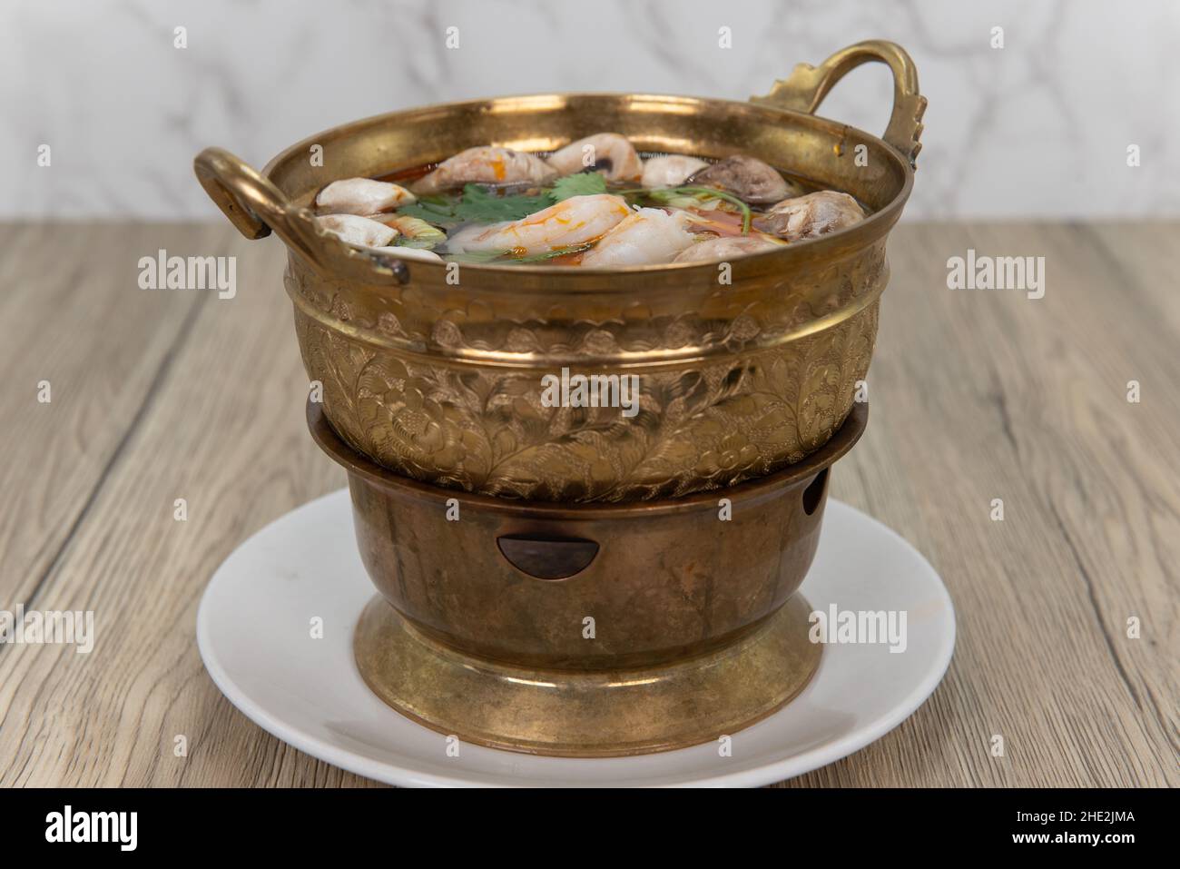 Kunstvoll verzierte Messingschüssel mit tom Yung goong Garnelensuppe, heiß und bereit zum Schlürfen serviert. Stockfoto