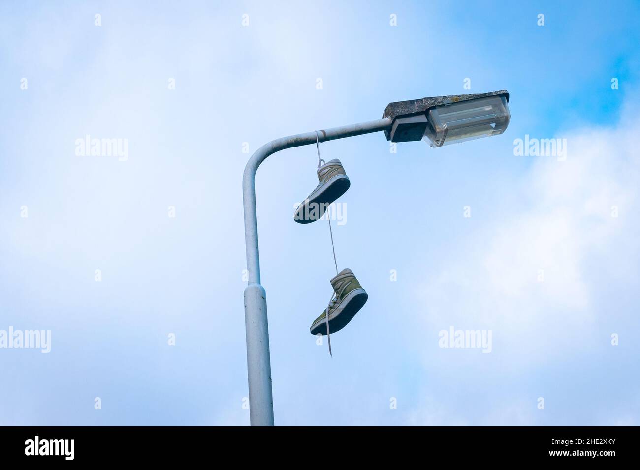 Sportschuhe, die als Witz an einem Laternenpfahl hängen, von unten mit teilweise bewölktem Himmel fotografiert. Stockfoto