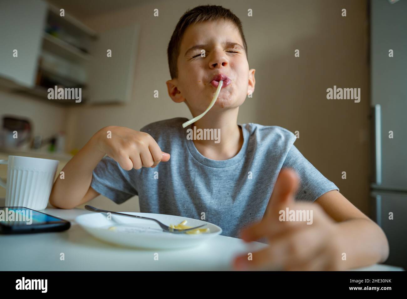 Junge, Kind, das Makkaroni isst, ziehen lange Pasta in den Mund Stockfoto