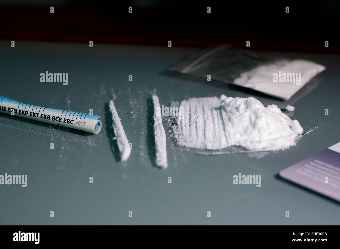 Umschlag, Stapel und gerollte Banknote. Kokain in Streifen auf einem hellen, gespiegelten Hintergrund unterteilt. Nahaufnahme. Betäubungsmittel-Konzept. Stockfoto
