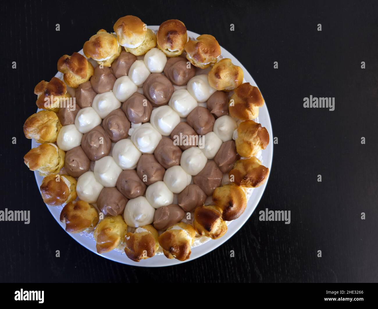 Flaches Foto einer saint honore-Torte auf einem weißen Teller, der auf einem schwarzen Holztisch ruht Stockfoto