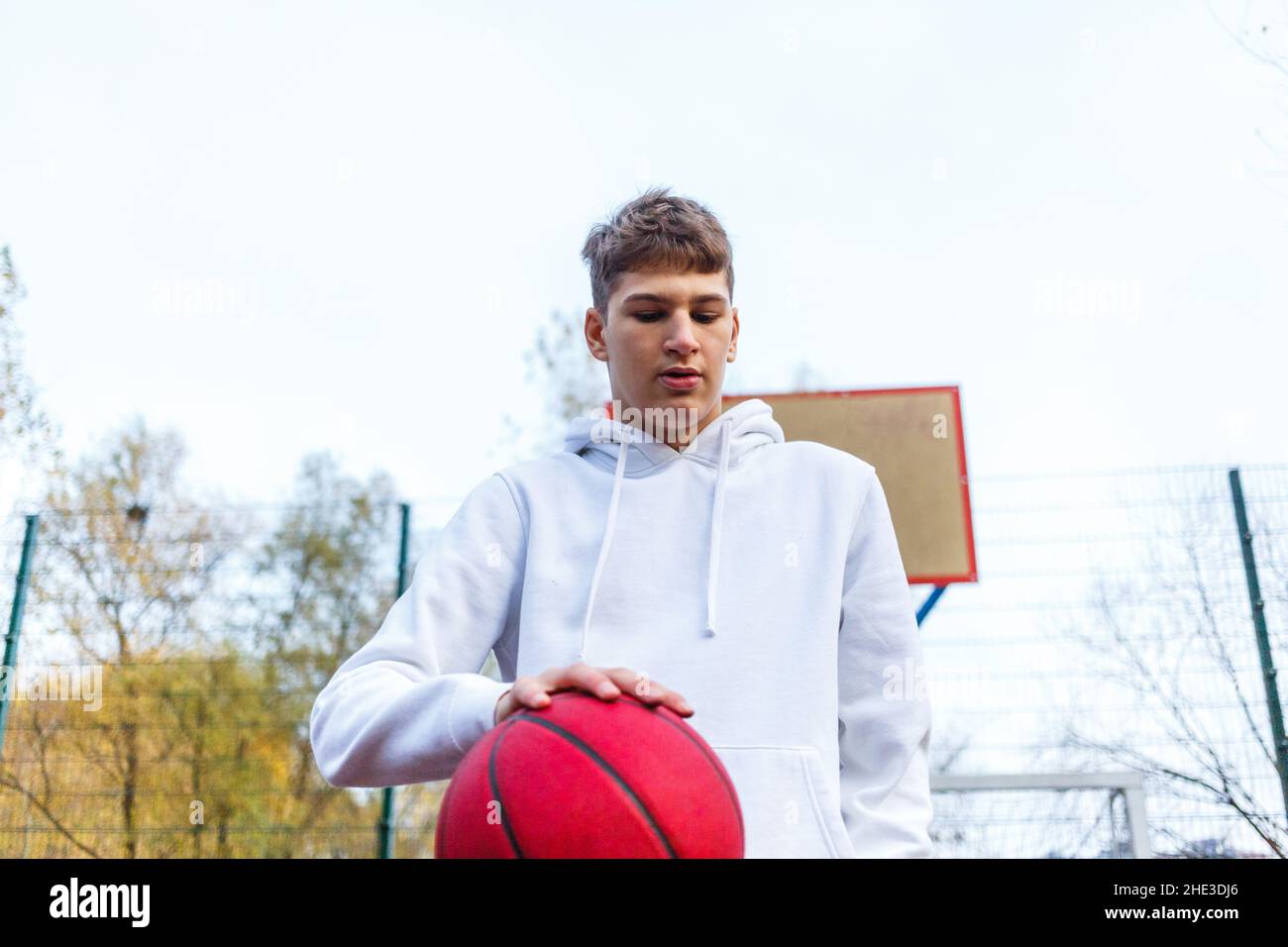 Netter Teenager im weißen Hoodie, der Basketball spielt. Kleiner Junge mit  roter Kugel, der Dribbeln lernt und auf dem Stadtplatz schießt. Hobby für  Kinder, aktives Leben Stockfotografie - Alamy