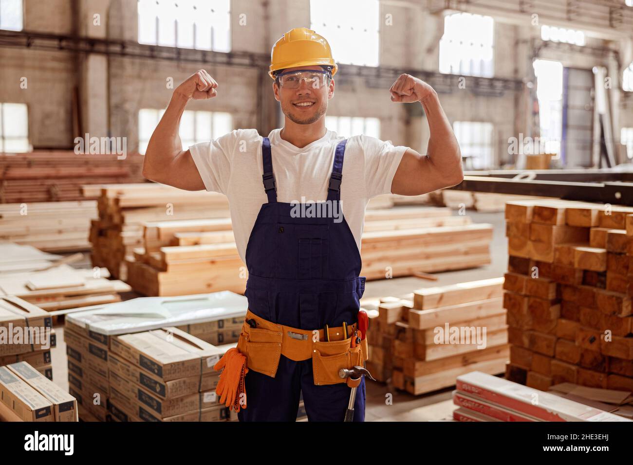 Fröhlicher männlicher Baumeister, der seine muskulösen Arme demonstriert Stockfoto