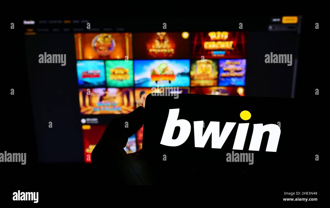 Person, die Mobiltelefon mit Logo der österreichischen Firma bwin Interactive Entertainment AG auf dem Bildschirm vor der Webseite hält. Konzentrieren Sie sich auf die Telefonanzeige. Stockfoto