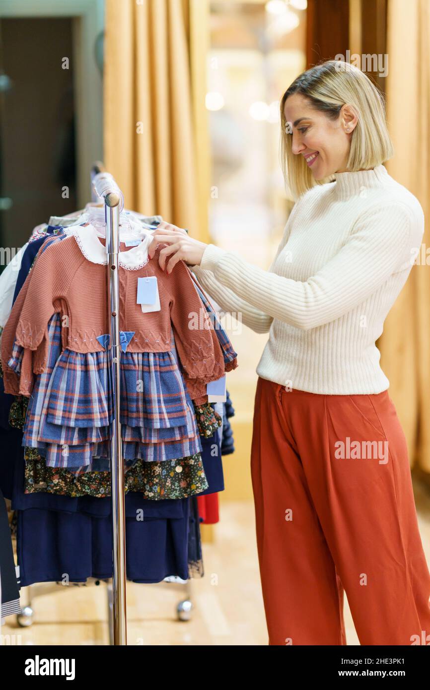Frau mittleren Alters, die Kleidung für ihre Kinder in einem Kinderbekleidungsgeschäft kauft. Stockfoto