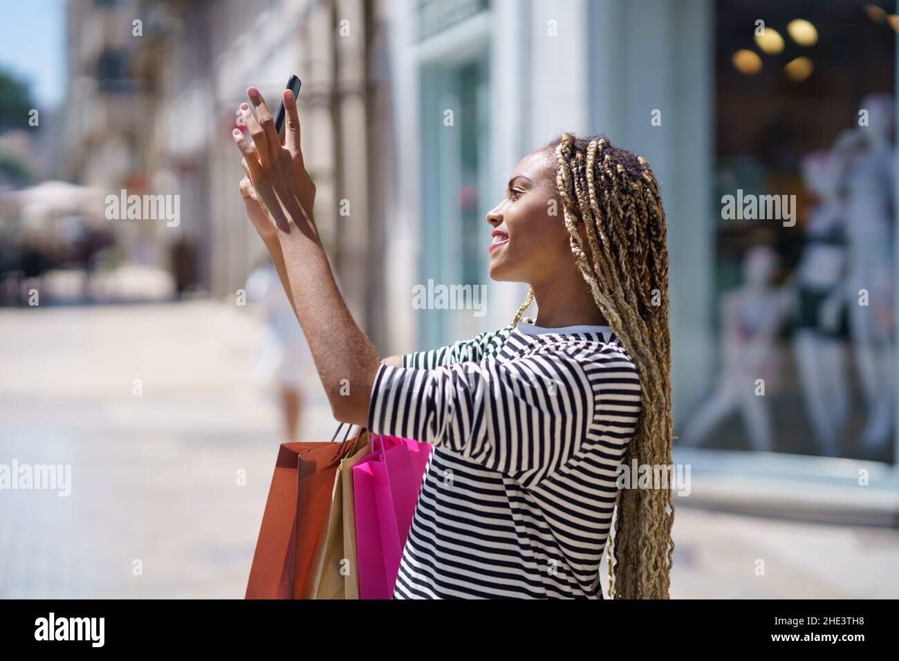 Junge schwarze Frau fotografiert mit ihrem Smartphone etwas in einer Einkaufsstraße. Stockfoto