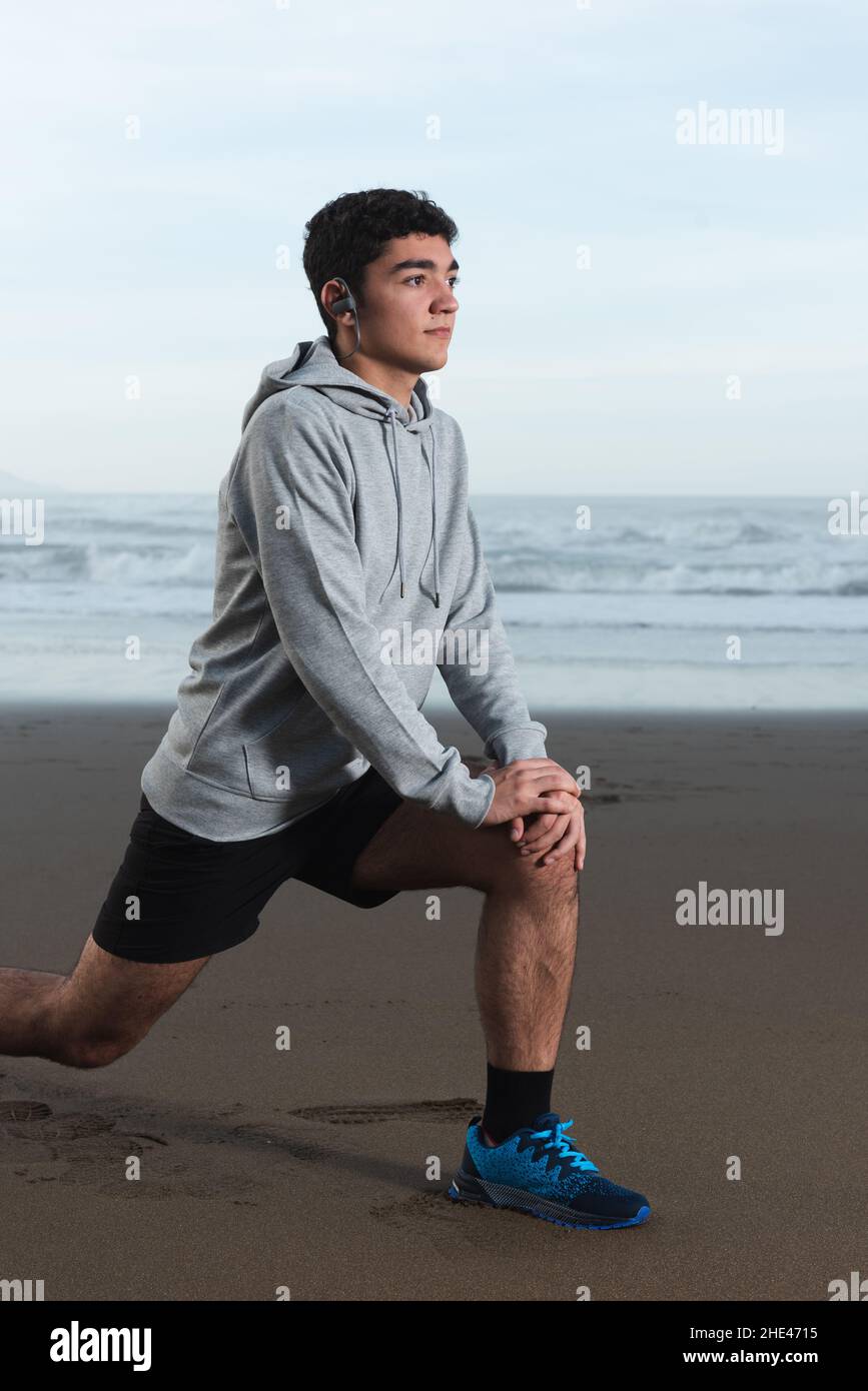 Hispanischer junger Mann, der Psoas streckte und sich am Strand aufwärmte. Stockfoto
