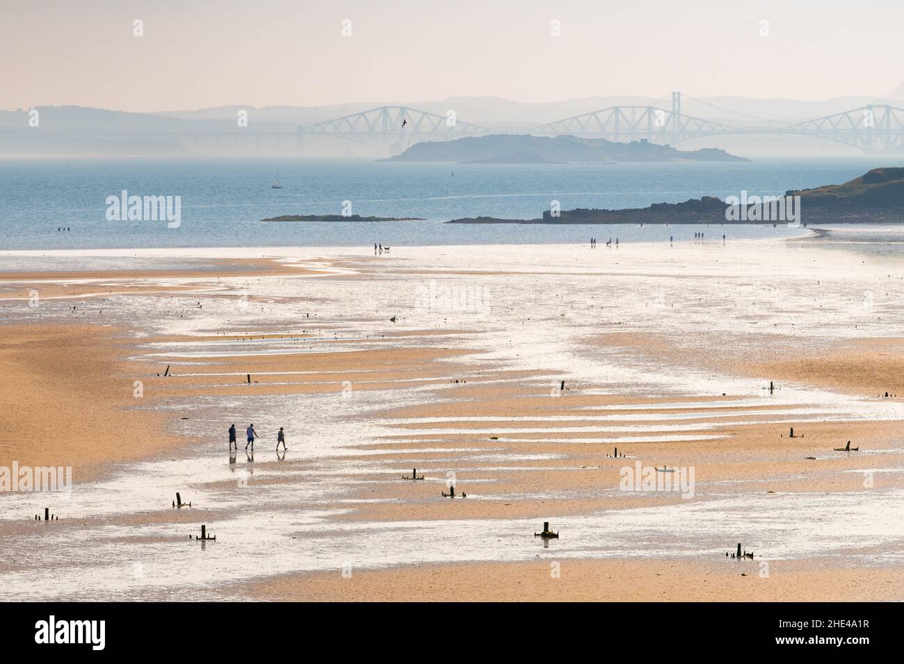 Figuren auf Pettycur Beach, Pettycur Bay, Kinghorn, Fife, Schottland, Großbritannien bei Ebbe mit Forth Road und Eisenbahnbrücken in der Ferne Stockfoto