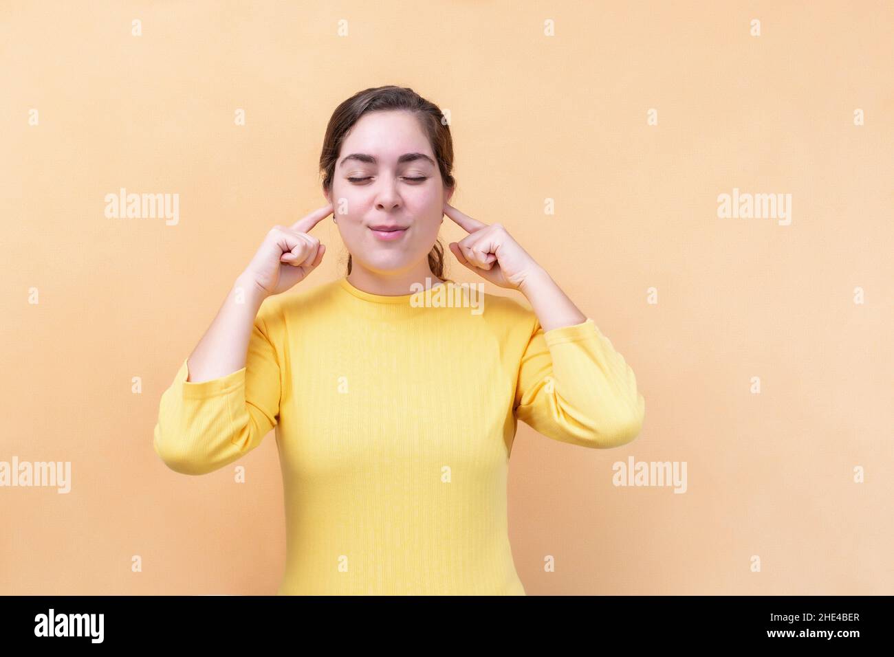 Frau, die die Finger in die Ohren klebt, hört nicht laute Geräusche, isoliert auf hellorangenen Hintergrund. Stockfoto