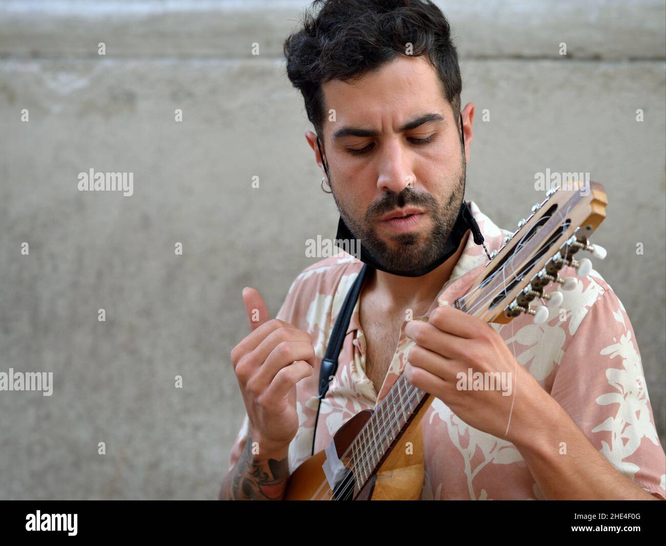 Ein hübscher junger Lateinamerikaner mit schwarzem Bart und Gesichtsmaske unter dem Kinn spielt eine kleine Andengitarre (Charango) mit zehn Saiten. Stockfoto