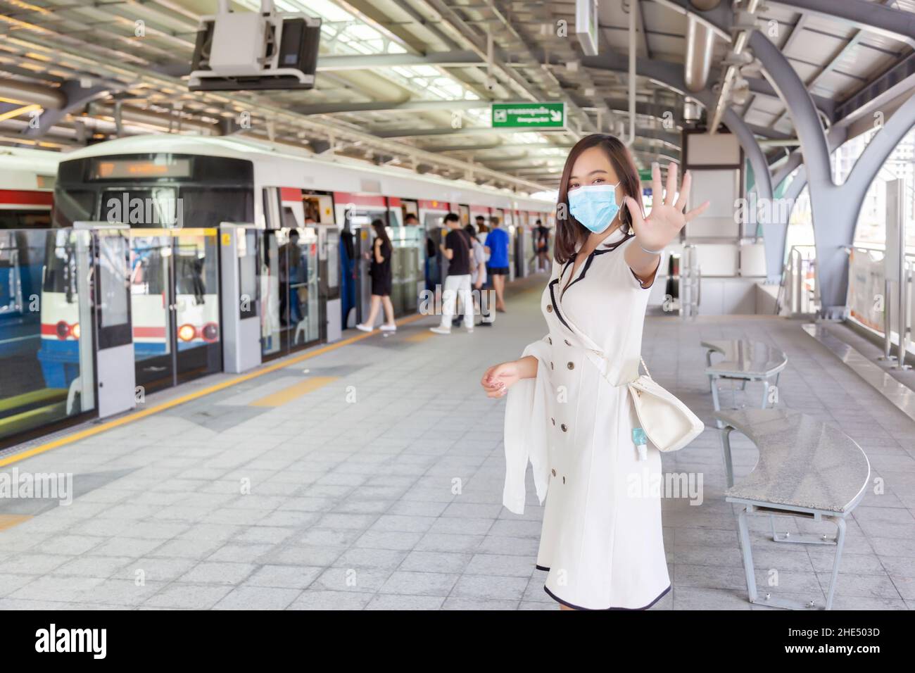 asiatische Frau mit medizinischer Maske in neuer normaler Weise auf Coronavirus-Ära. Die Frau zeigt Hand in Auf Wiedersehen Aktion Skytrain auf Raiway Station. Stockfoto