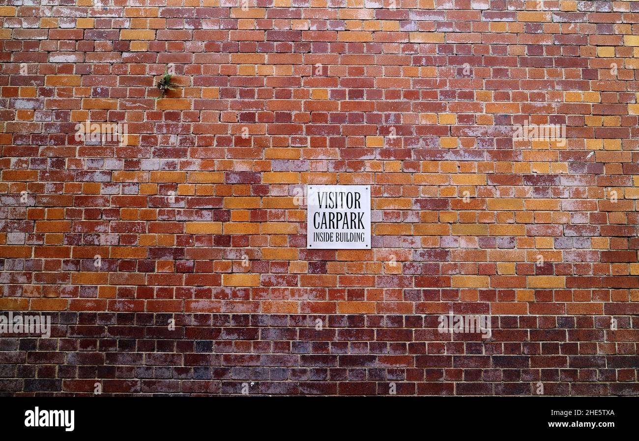 Metallisches Besucherparkschild an der denkmalgeschützten alten mehrfarbigen Backsteinmauer in Brisbane, Australien Stockfoto