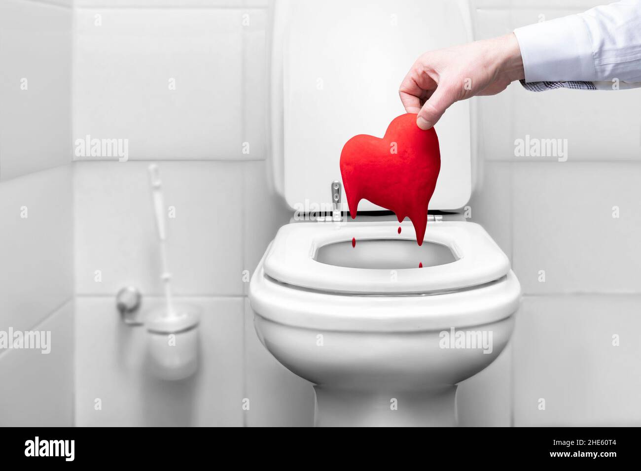 Die Hand eines Mannes wirft ein blutiges Herz in die Toilette, ein Symbol der Liebe. Das Ende der Trennung der Beziehung, traurige valentine. Streitereien und Auflösung von r Stockfoto