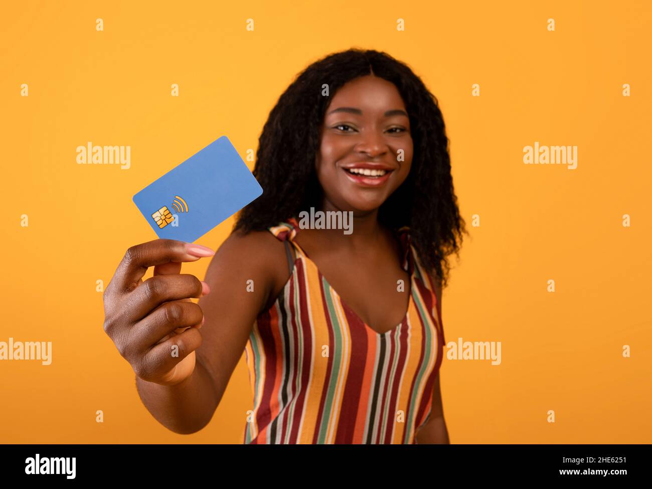 Schöne schwarze Frau zeigt Kreditkarte auf orangefarbenem Hintergrund, selektiver Fokus. Kontaktloses Einkaufen, Fernbanking Stockfoto