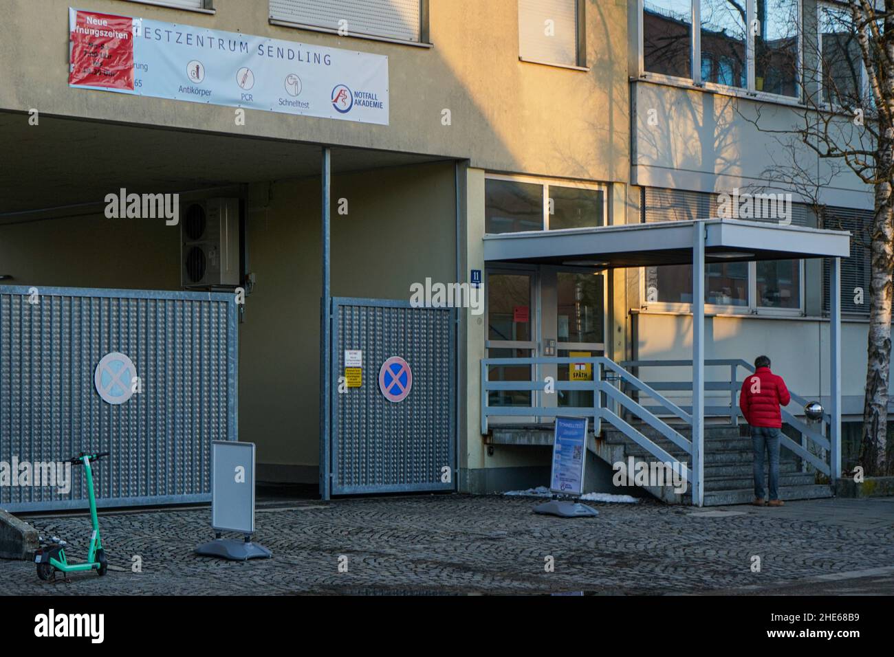 Ein Mann in einer roten Jacke wartet rauchend vor einem Corona Testcenter in München Sendling. Stockfoto