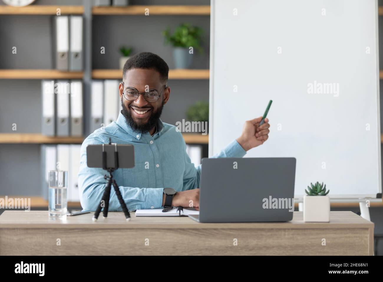 Freundlich fröhlich tausendjährigen afroamerikanischen Mann Tutor zeigen, um englische Regeln, schaut auf pc und Smartphone Webcam Stockfoto