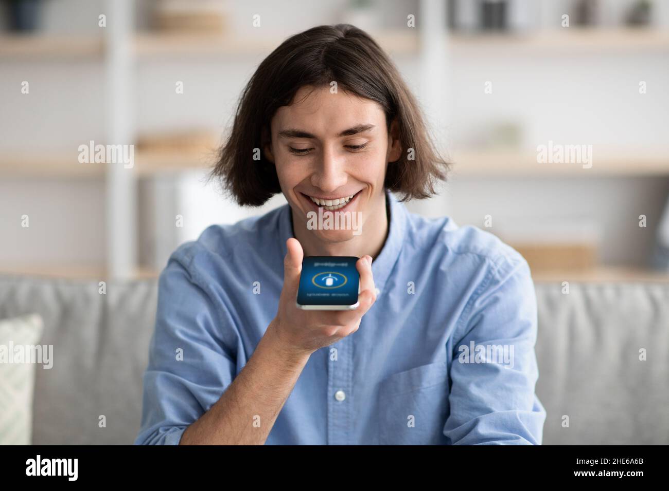 Junger Mann mit Smartphone Voice Assistant Online-Service, Sprachnachrichten aufzeichnen, sitzen auf dem Sofa zu Hause Stockfoto