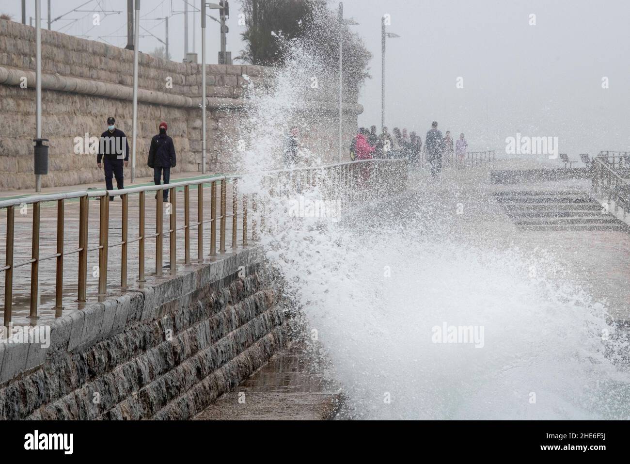 Eine Welle stürzt auf einem Gehweg in der Nähe einiger Fußgänger an der Küste von Cascais ab. Portugal verzeichnete seit Beginn der Pandemie 1.577.784 Fälle und 19.071 Todesfälle im Zusammenhang mit Covid-19, so das Bulletin der Generaldirektion Gesundheit (DSG). Stockfoto