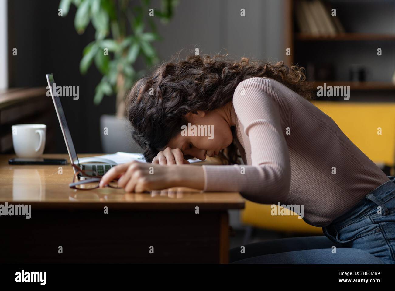Burnout für die Arbeit. Müder weiblicher Angestellter, der den Kopf auf den Tisch legt und unter chronischem Arbeitsdruck leidet. Stockfoto