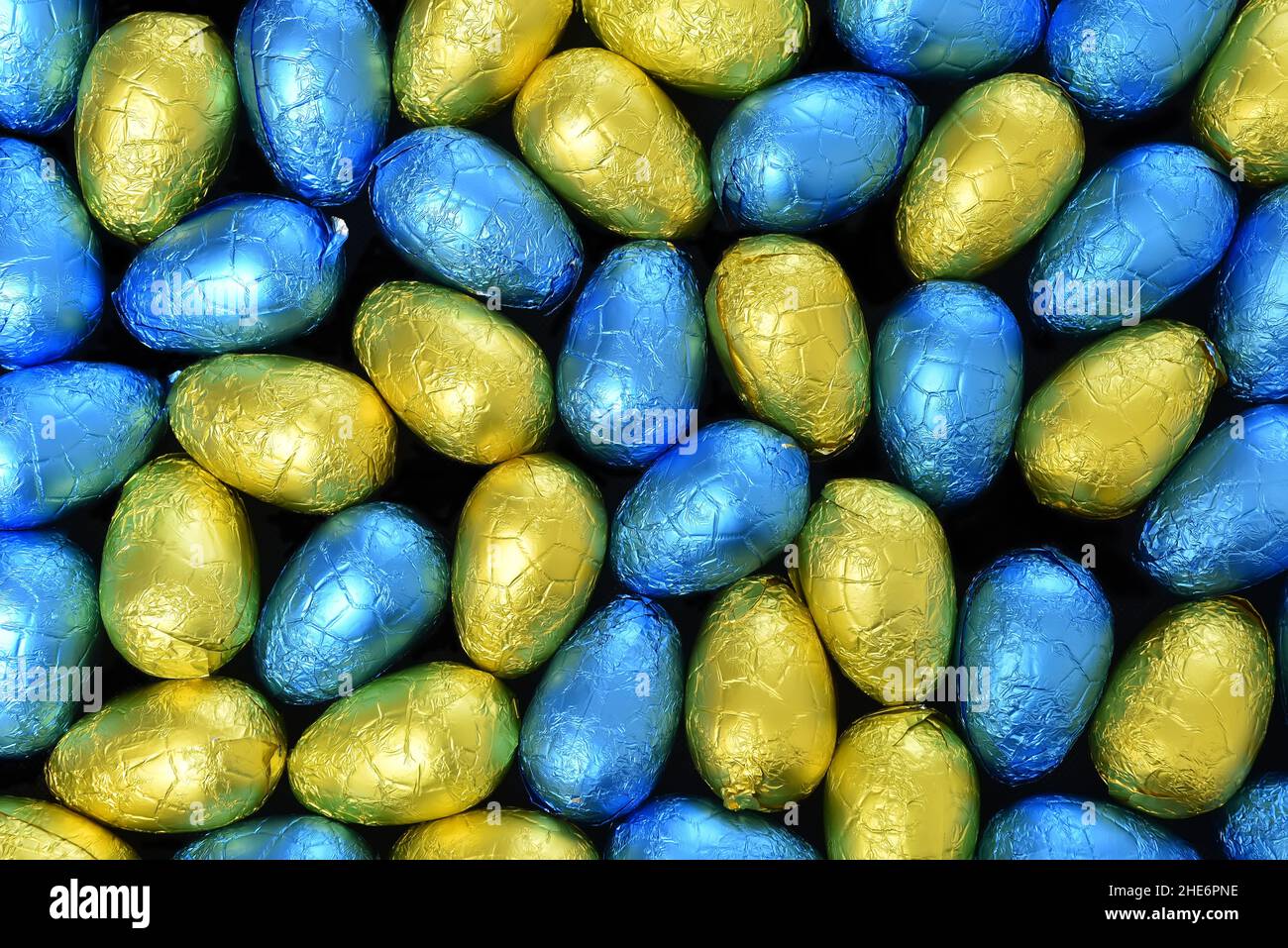 Stapel oder Gruppe von mehrfarbigen und verschiedenen Größen von bunten Folie verpackt Schokolade ostereier in blau, gelb und lindgrün. Stockfoto