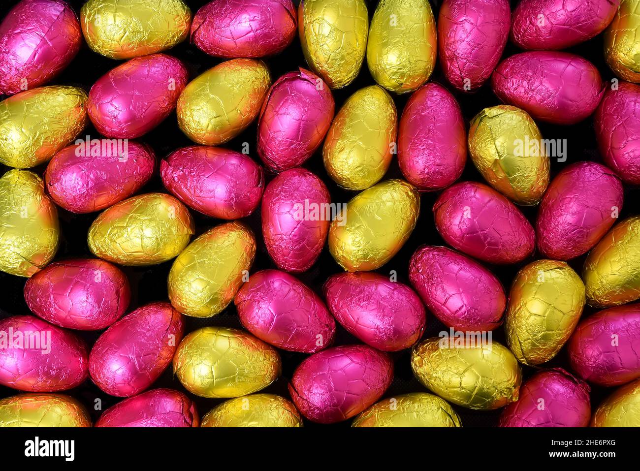 Stapel oder Gruppe von mehrfarbigen und verschiedenen Größen von bunten Folie verpackt Schokolade ostereier in gelb, Gold und rosa. Stockfoto