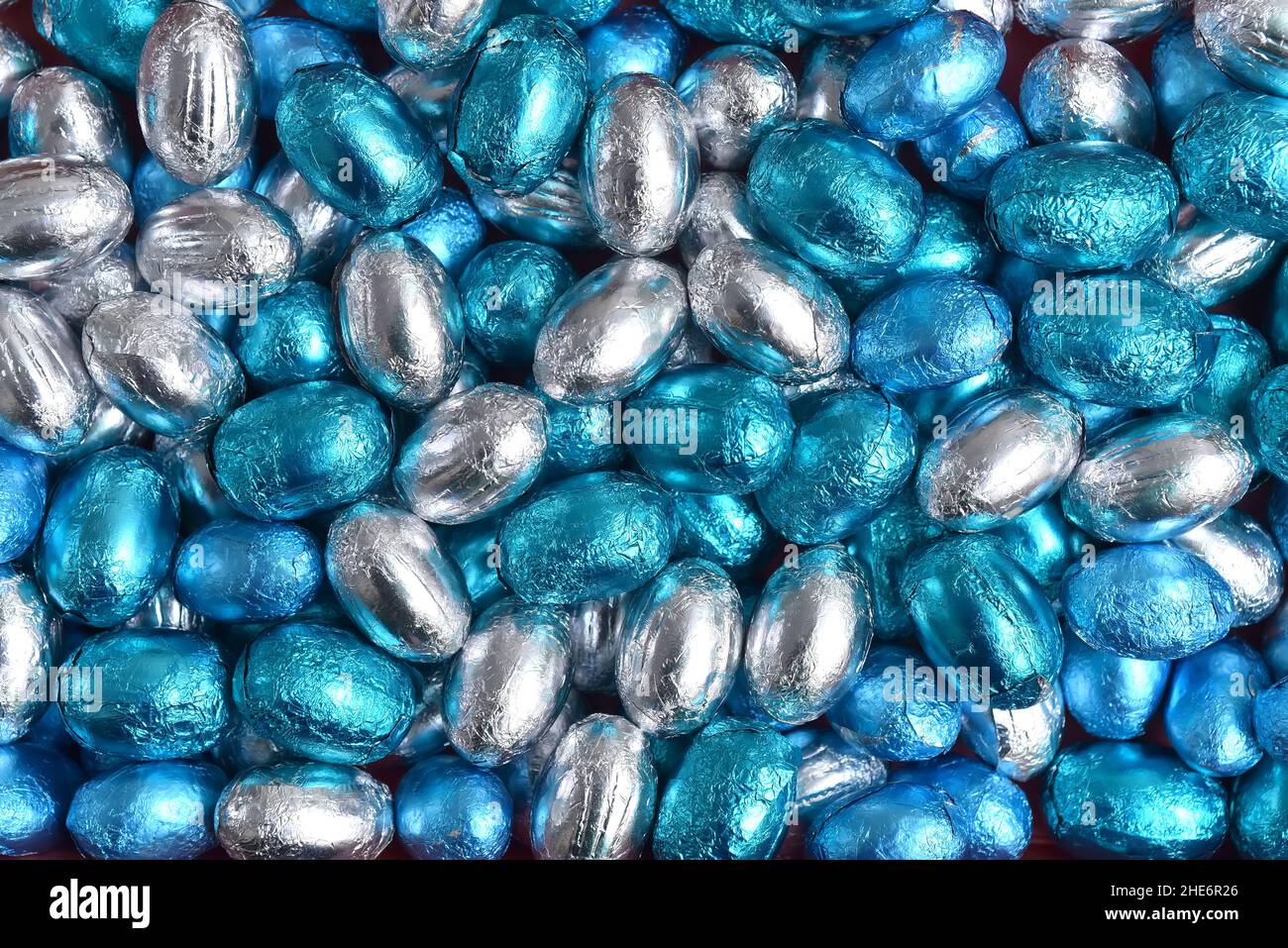 Blaue, silberne und türkisfarbene Schokoladen-ostereier in Folienverpackung vor schwarzem Hintergrund. Stockfoto