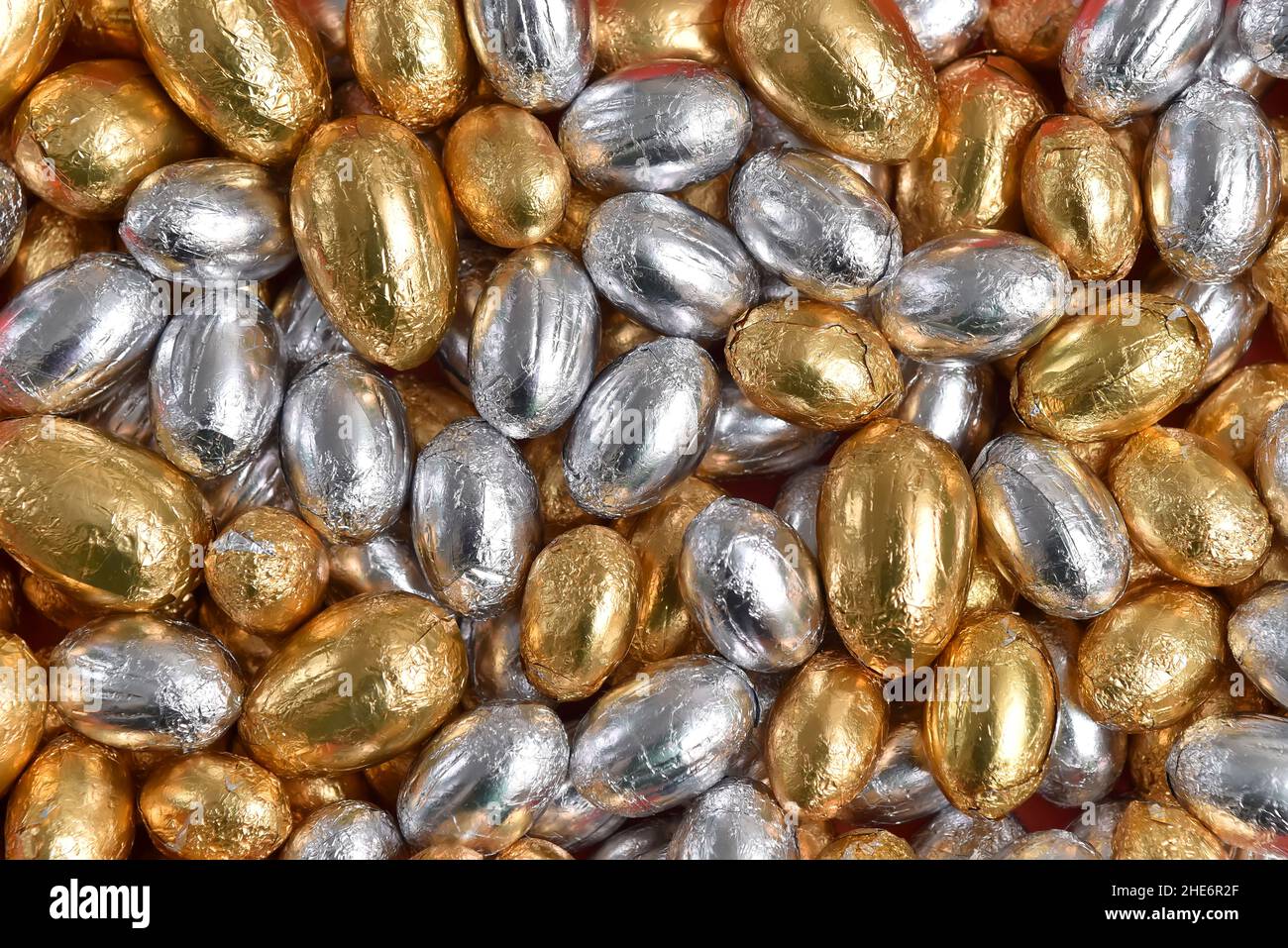 Große und kleine, in Gold und Silber verpackte Ostereier aus Schokolade vor einem rosa, pfirsichfarbenen Hintergrund. Stockfoto