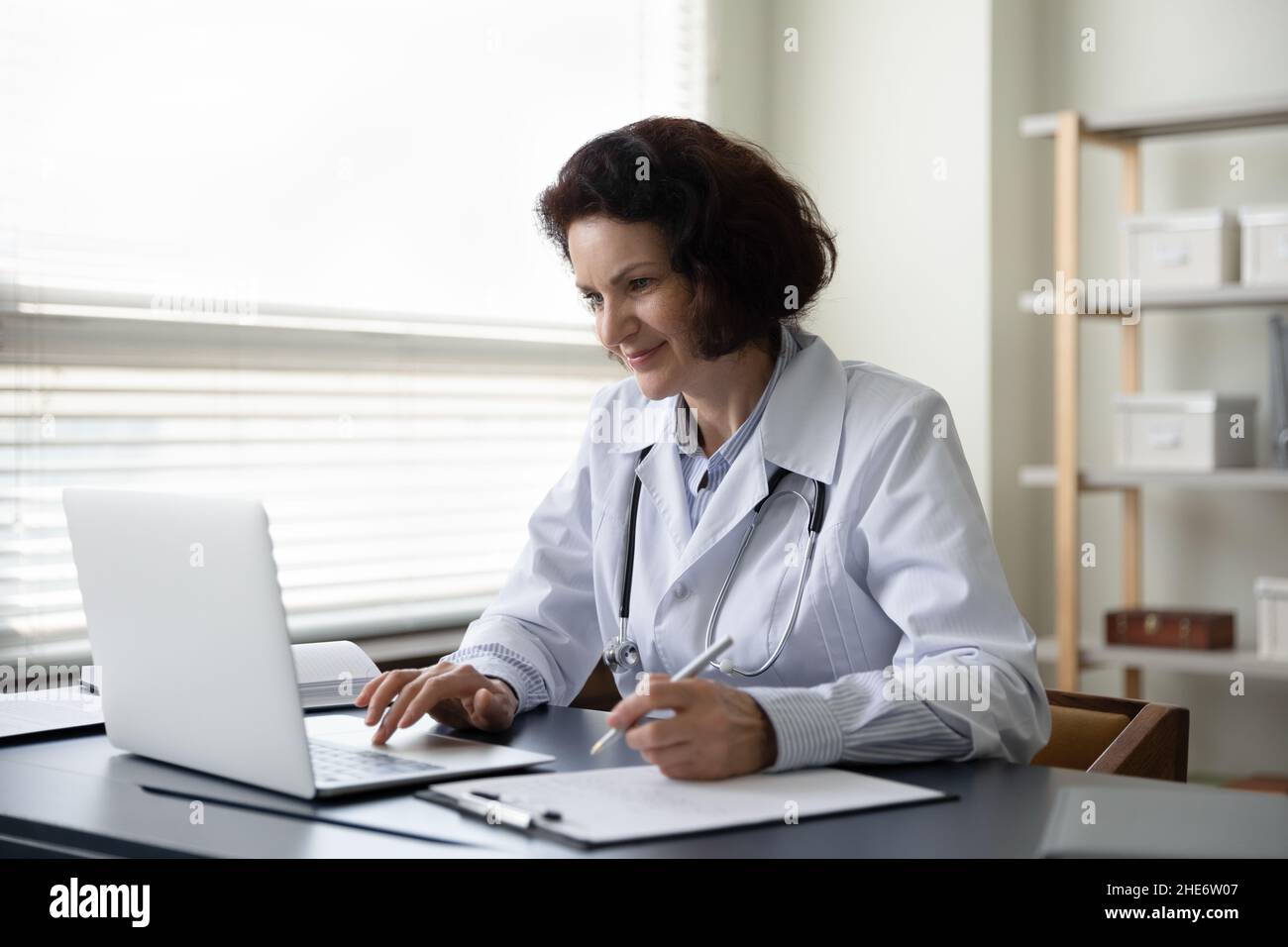 Glückliche alte reife weibliche Ärztin, die im Klinikbüro arbeitet. Stockfoto
