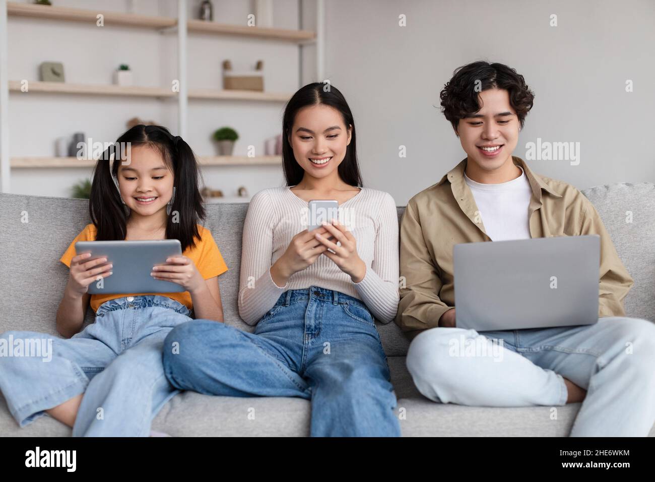 Lächelndes Teenager-Kind und junge asiatische Mutter und Vater surfen im Internet, chatten auf Gadgets, spielen Spiel Stockfoto