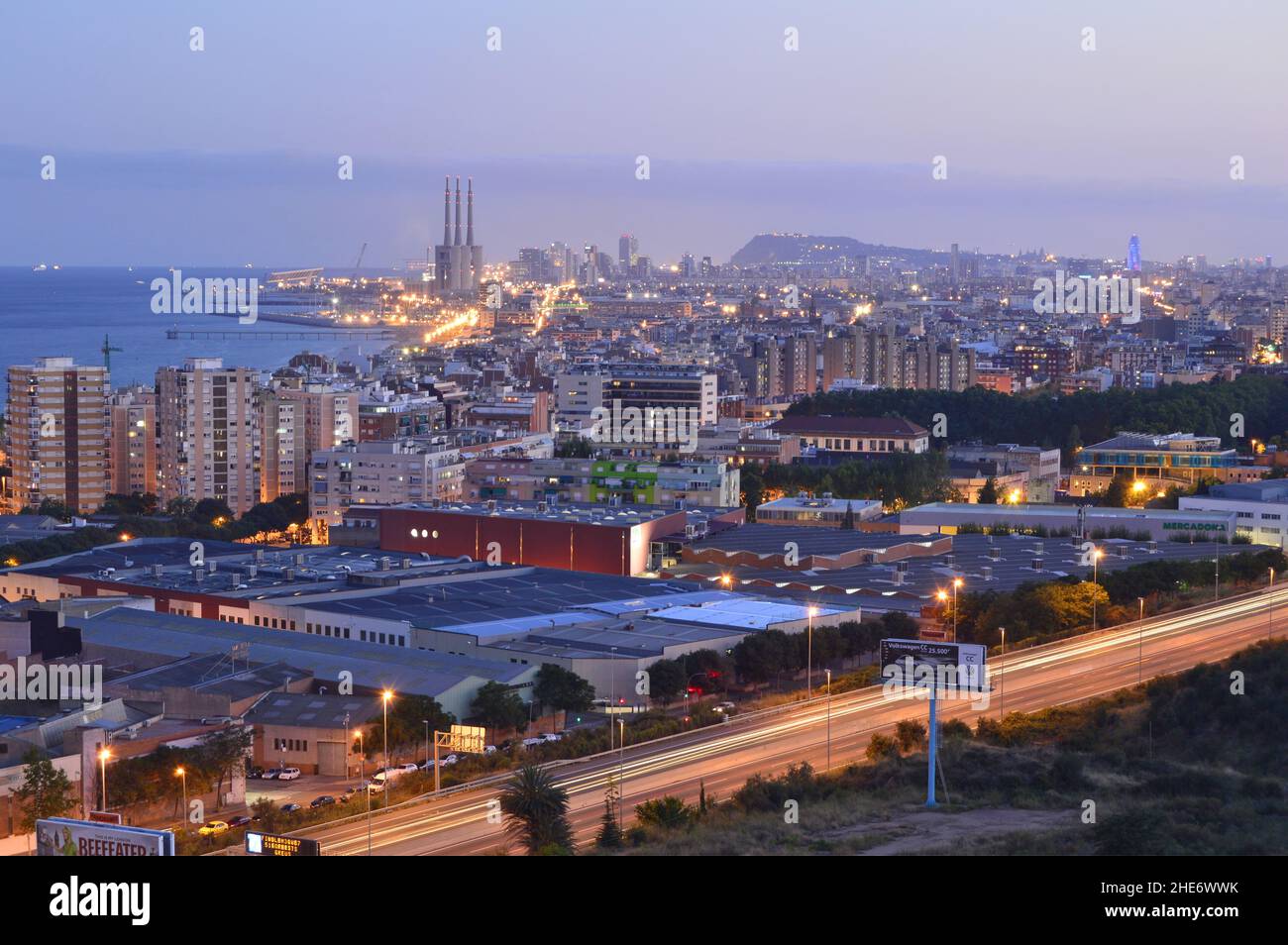 Industrieller Vorort von Badalona mit Lagerhäusern und der Stadt Barcelona im Hintergrund, erhöhte Ansicht in der Dämmerung, Katalonien Spanien. Stockfoto
