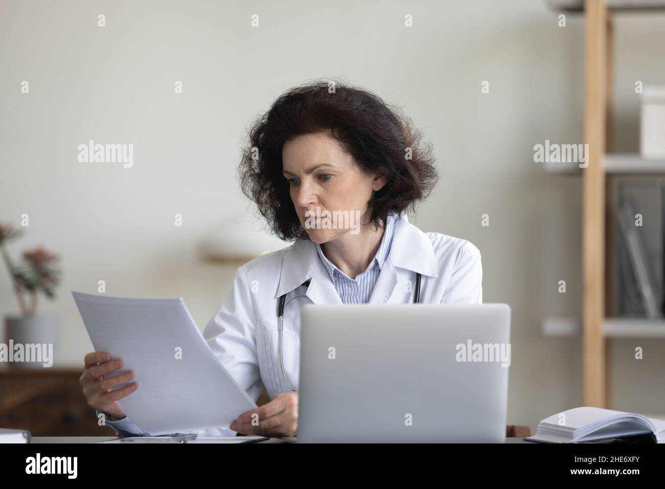 Konzentrierte alte Ärztin beim Lesen des Papierdokuments. Stockfoto Konzentrierte alte Ärztin beim Lesen des Papierdokuments. Stockfoto