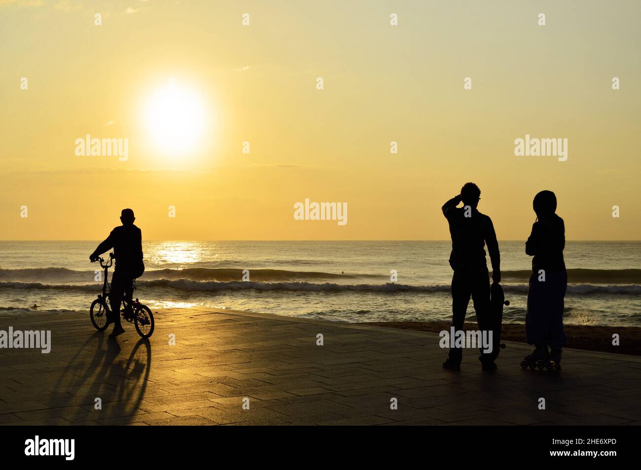 Die Menschen haben sich gegen die Morgensonne auf der gepflasterten Promenade am Strand von Barceloneta in Barcelona, Spanien, geschildet. Stockfoto