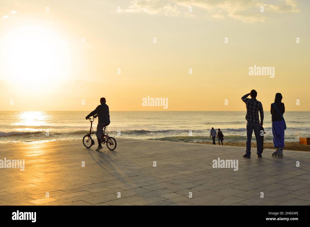 Die Menschen haben sich gegen die Morgensonne auf der gepflasterten Promenade am Strand von Barceloneta in Barcelona, Spanien, geschildet. Stockfoto