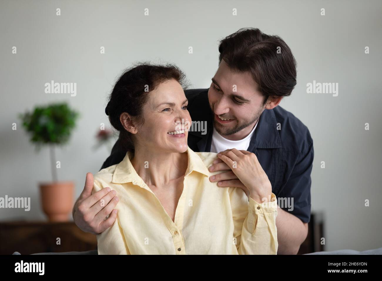 Liebevoller junger Mann, der zu Hause ältere Mutter kuschelt. Stockfoto