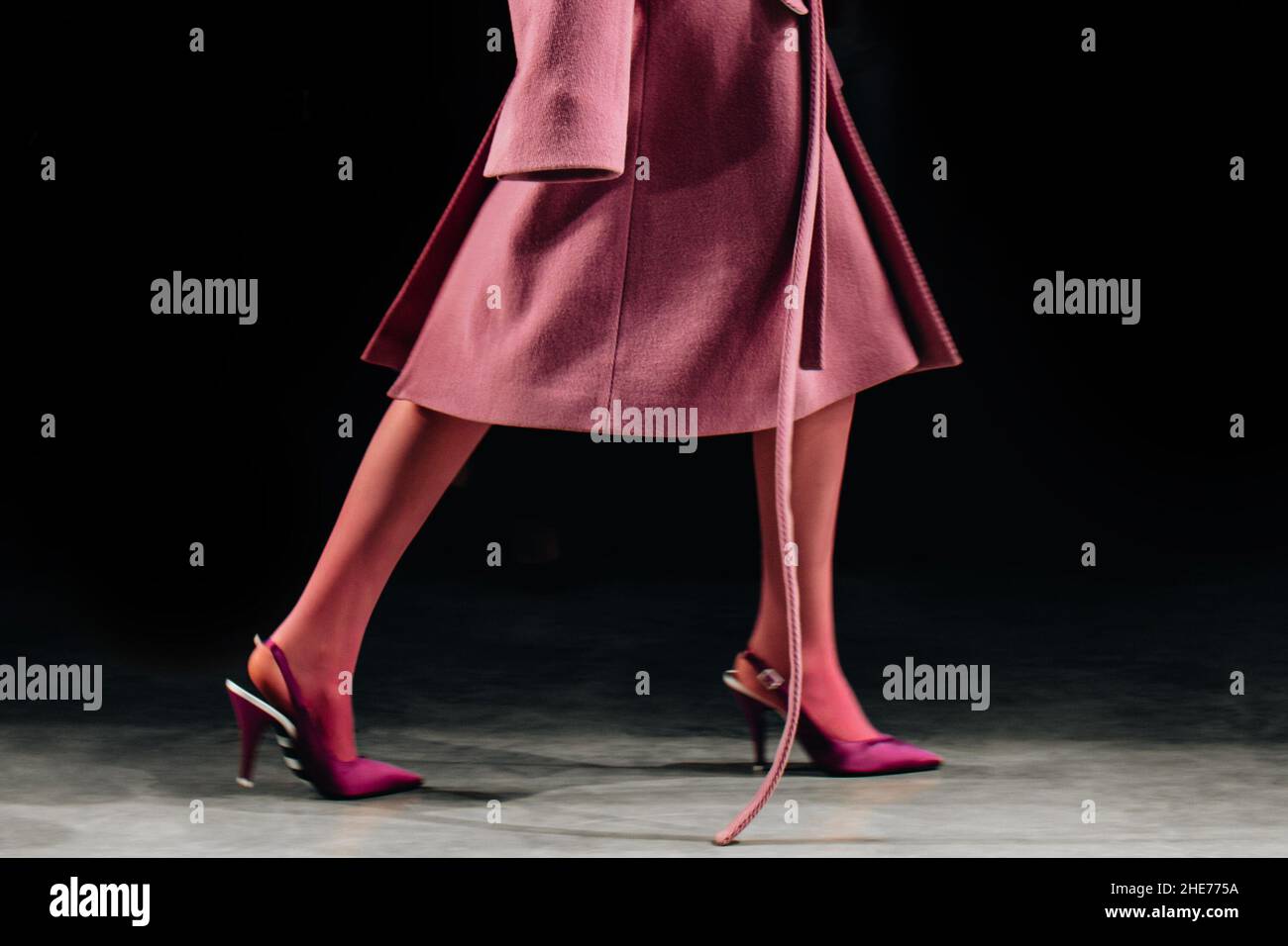 Kurze weibliche Figur, gekleidet in klassischen langen rosa Fancy Mantel und High Heels, die auf schwarzem Hintergrund über die Landebahn laufen Stockfoto