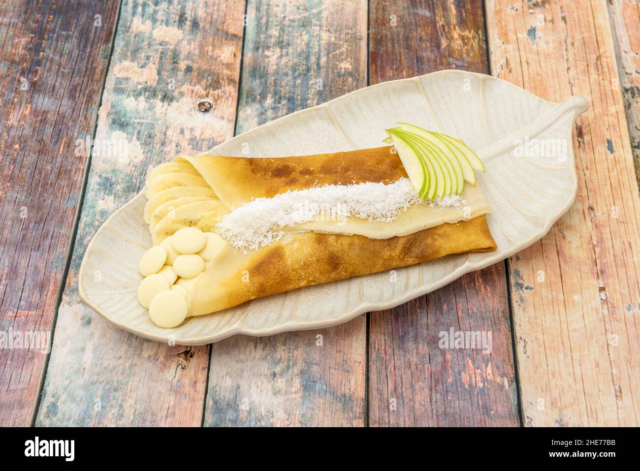 Französisches Crepe Dessert gefüllt mit Banane und Apfel mit weißer Schokolade und geriebener Kokosnuss Stockfoto