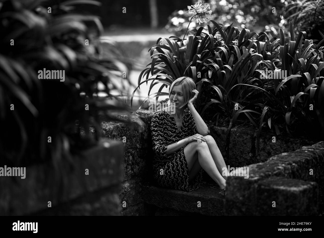 Eine junge Frau, die auf einer Steinbank in einem alten portugiesischen Park sitzt. Schwarzweiß-Foto. Stockfoto