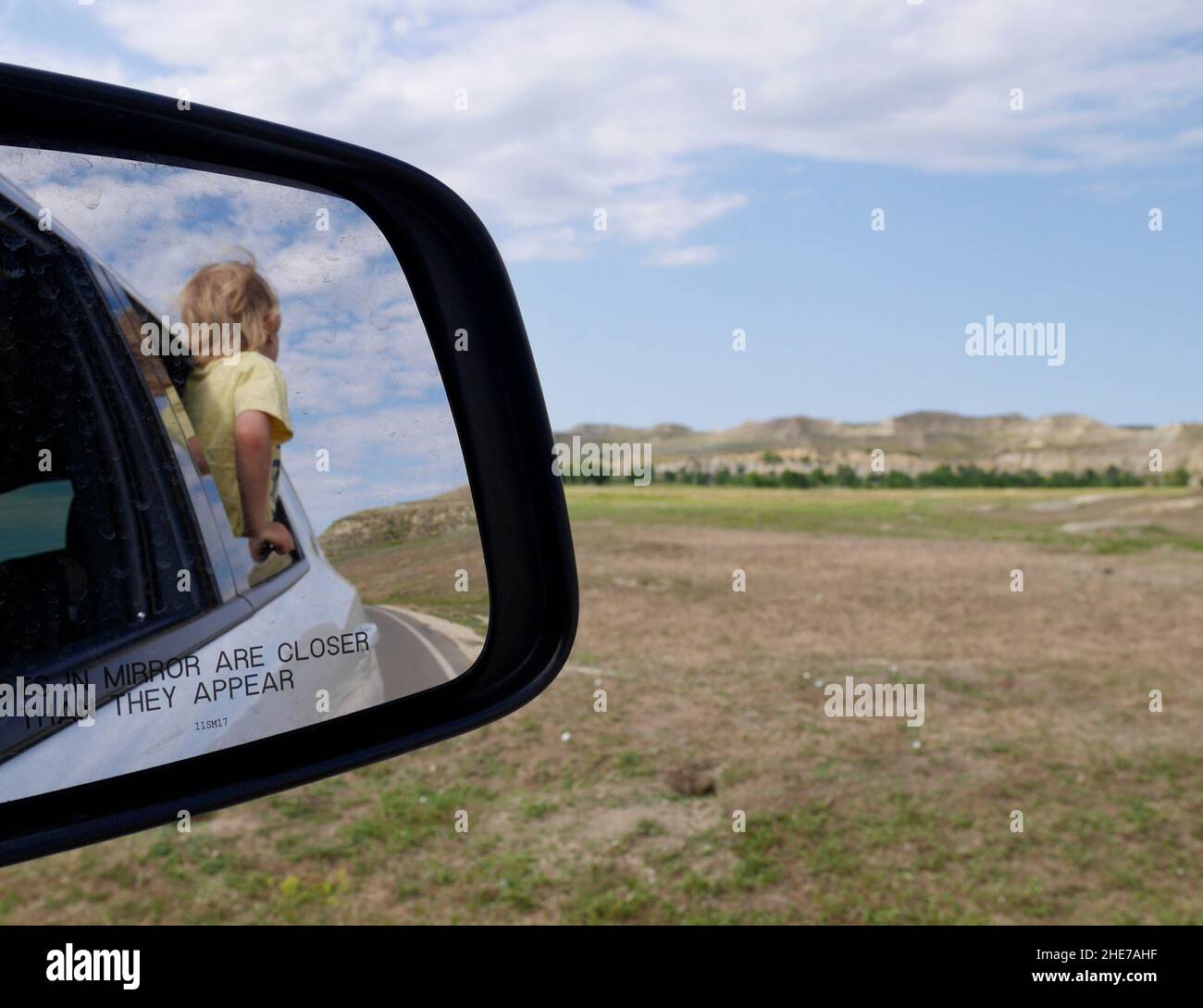 Spiegelbild eines Kindes im Rückspiegel, das aus dem Auto schaut und Badlands im Theodor Roosevelt National Park genießt. North Dakota, USA. Stockfoto