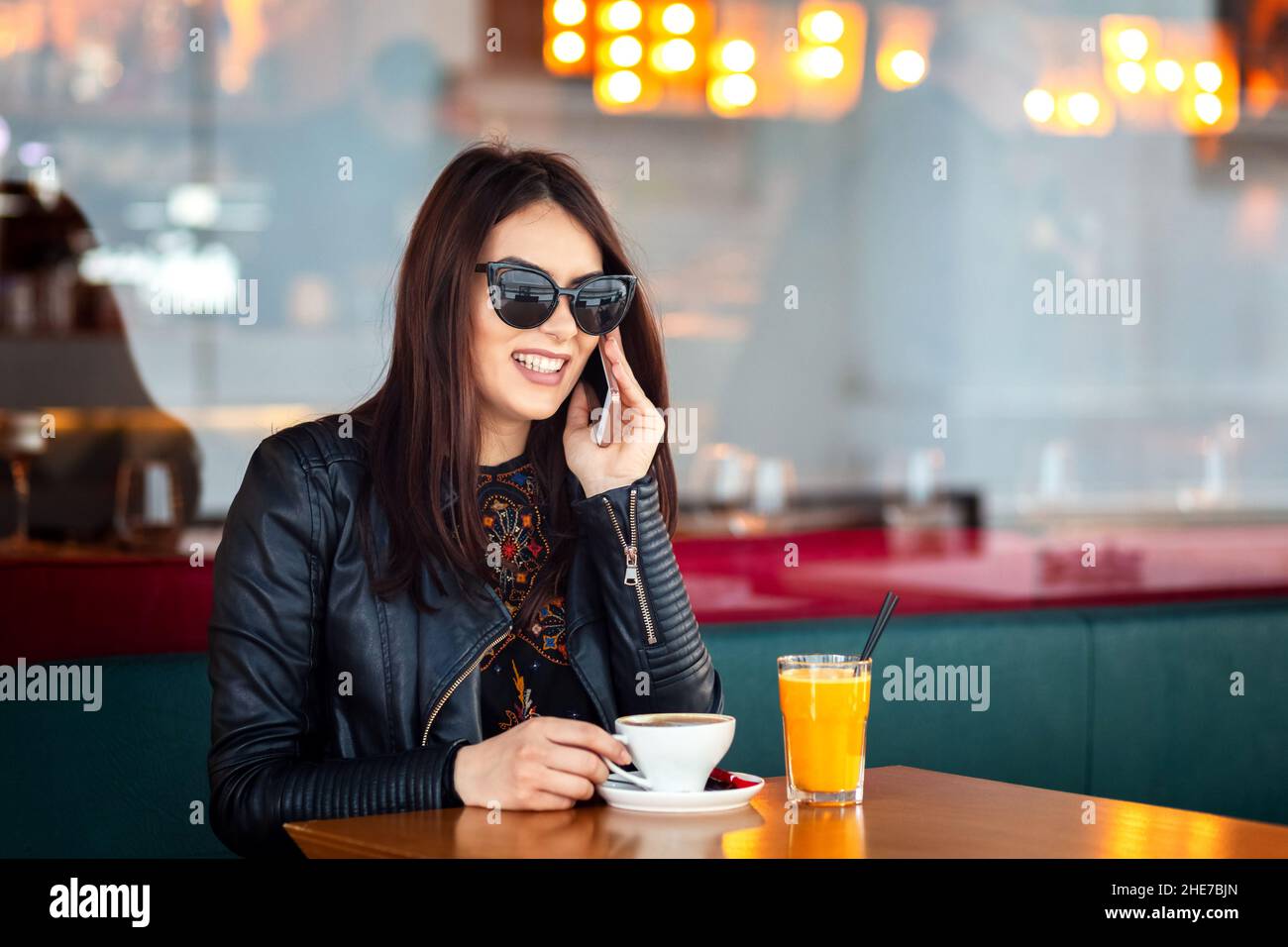 Fröhliche junge Frau im Café, die Kaffee trinkt und sich mit dem Handy unterhält Stockfoto