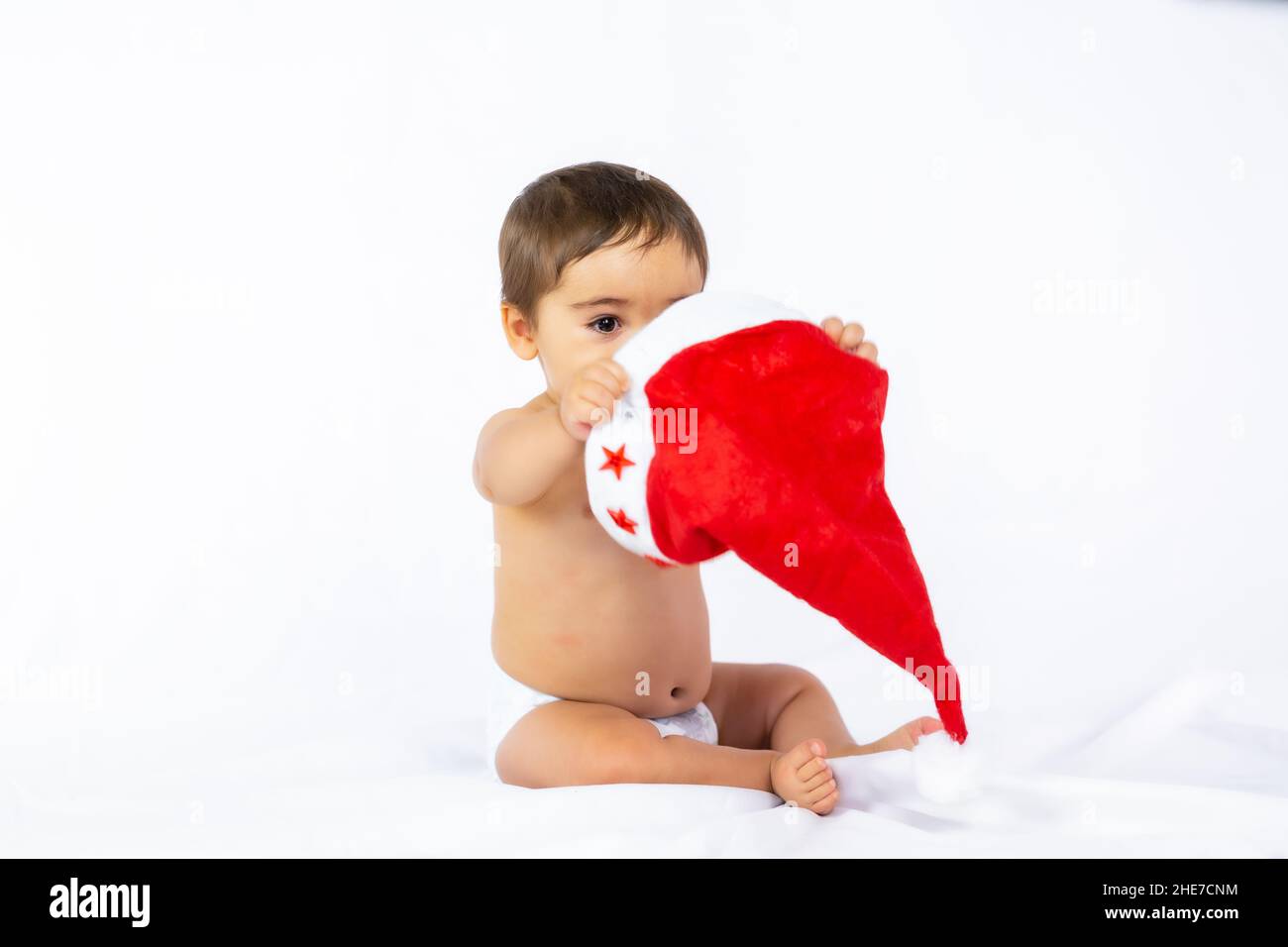 Ein kleiner Junge mit einem roten Weihnachtshut auf weißem Hintergrund, Platz kopieren und mit dem Hut des Weihnachtsmanns spielen Stockfoto
