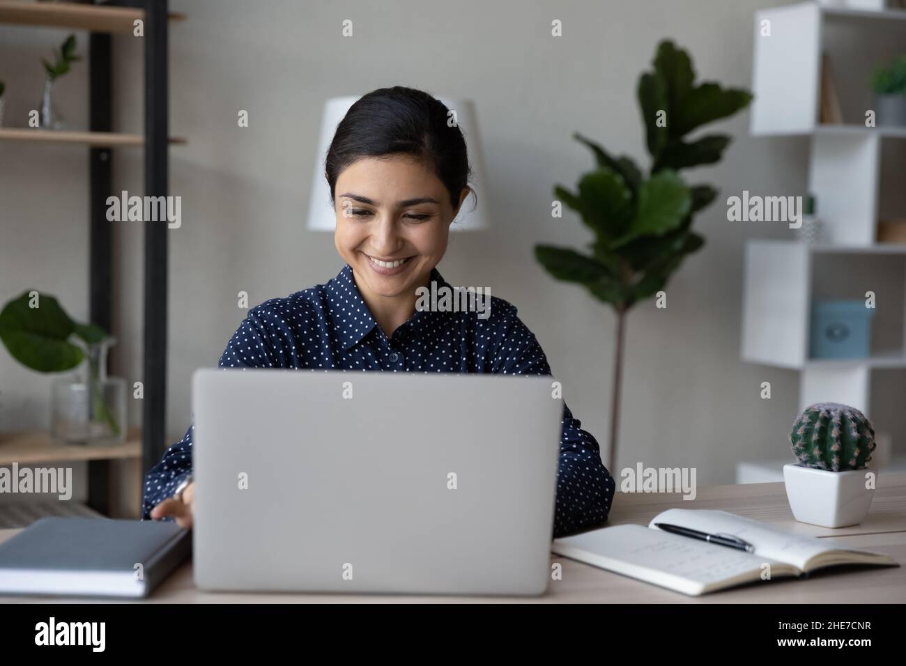 Fröhlicher indischer Büroangestellter, der am Tisch auf einem Laptop tippt Stockfoto