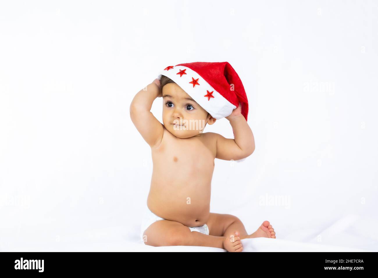 Ein kleiner Junge mit einem roten Weihnachtshut auf weißem Hintergrund, Platz kopieren und den Weihnachtsmann-Hut ausziehen Stockfoto
